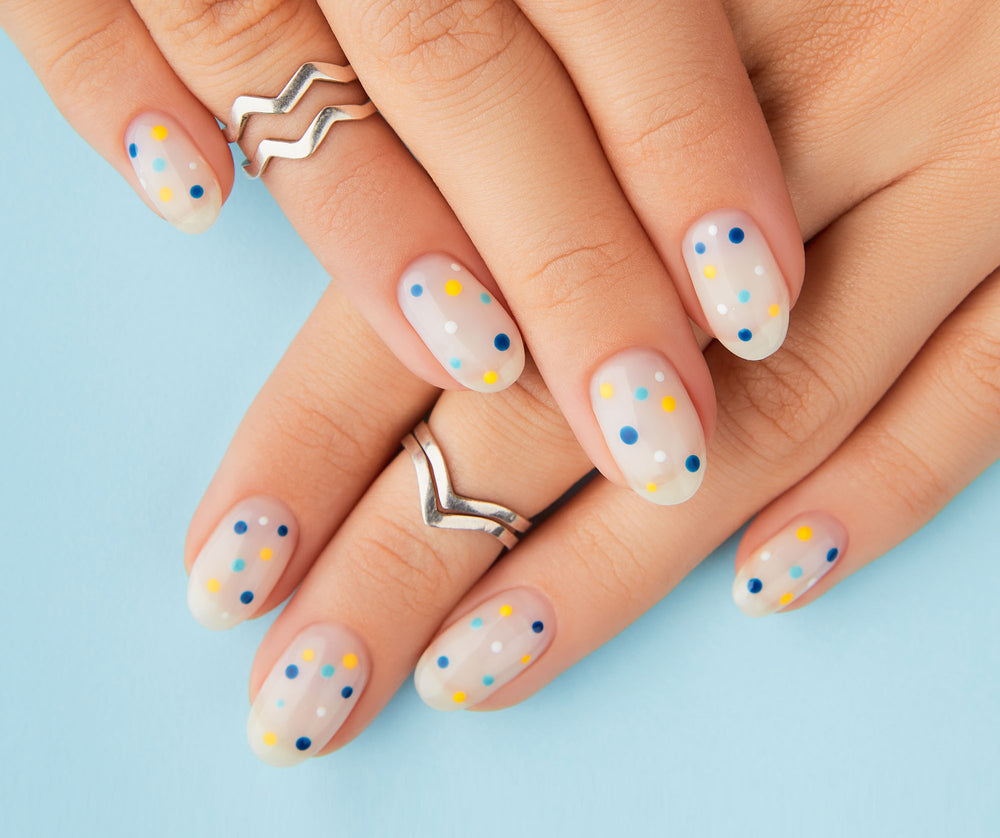Close-up of hands with polka dot nail design and silver rings on a light blue background