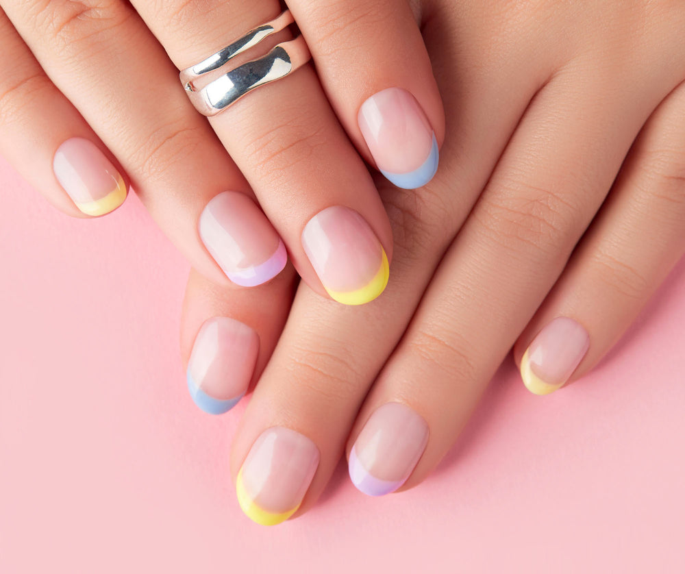 Close-up of hands with pastel nail polish on a pink background