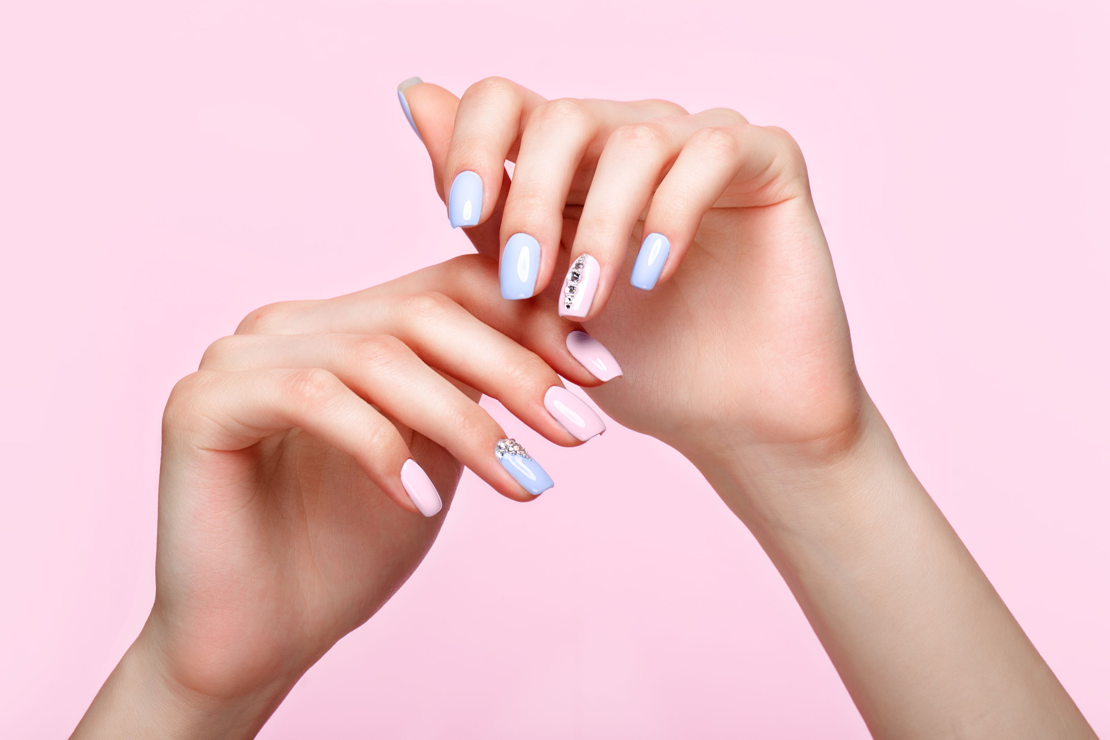 Close-up of hands with pastel nail polish on a pink background