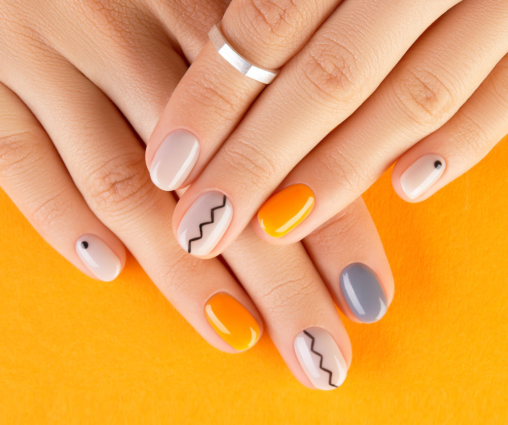 Close-up of hands with colorful nail designs on an orange background